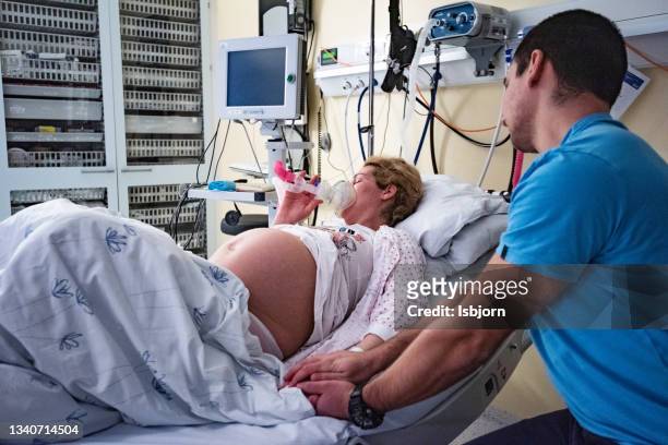 woman is using laughing gas for labouring in delivery room and  holding husband's hand. - childbirth stock pictures, royalty-free photos & images