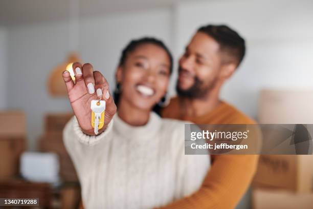 shot of a young couple hugging while showing their new house keys at home - real estate stock pictures, royalty-free photos & images