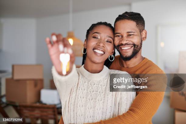 shot of a young couple hugging while showing their new house keys at home - moving house stock pictures, royalty-free photos & images