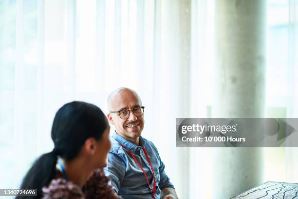 businessman wearing glasses listening to female colleague - candid office fotografías e imágenes de stock