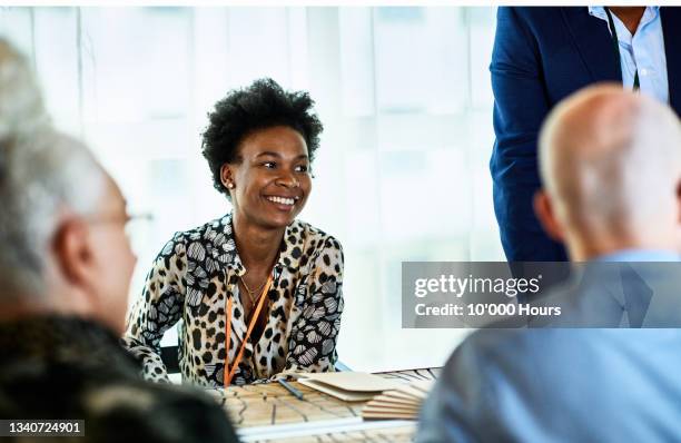 candid portrait of mid adult black businesswoman smiling in meeting - talking women office stockfoto's en -beelden