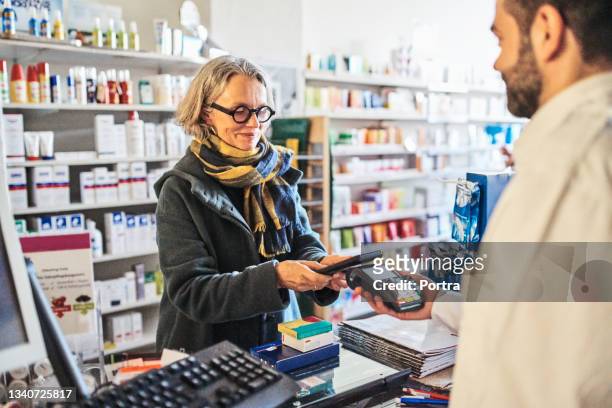woman paying for medicines at checkout in pharmacy - pharmacy stockfoto's en -beelden