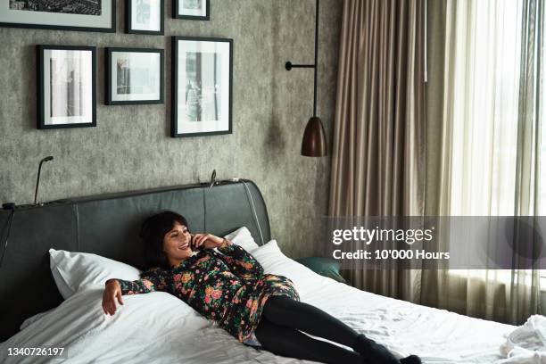 cheerful young woman relaxing on hotel bed using phone - king size bed stockfoto's en -beelden