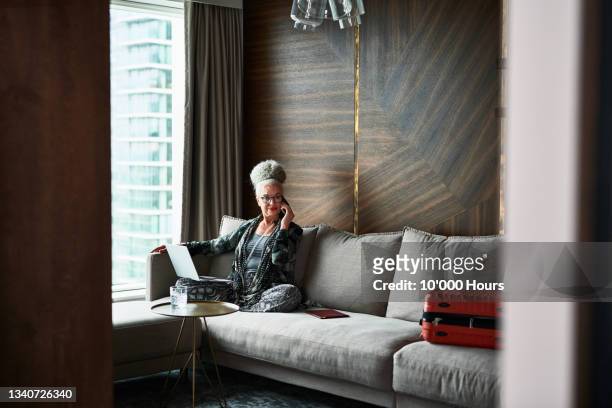 senior woman using phone and laptop in boutique hotel - business woman suitcase stockfoto's en -beelden