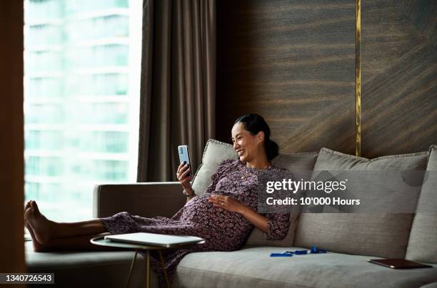 pregnant woman doing video call on phone in hotel room - asian woman pregnant stockfoto's en -beelden