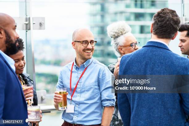 mid adult businessman enjoying beer on rooftop terrace with colleagues - feierabend stock-fotos und bilder