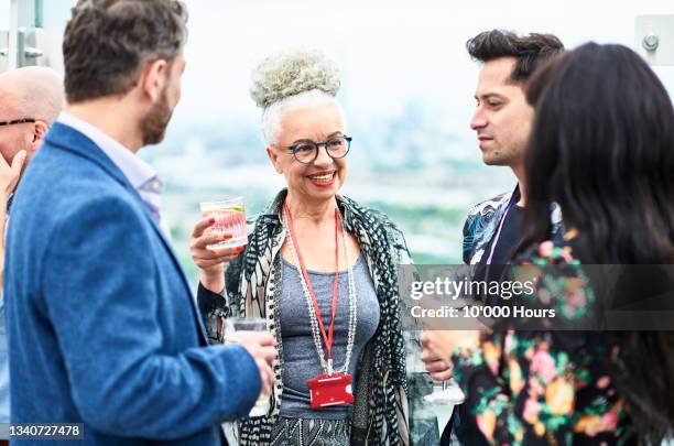 senior woman enjoying drinks with colleagues on rooftop terrace - outdoor business meeting stock pictures, royalty-free photos & images