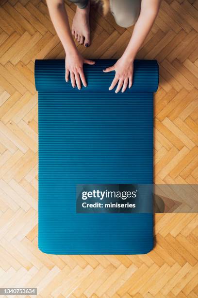 gros plan des mains féminines pliant un tapis d’exercice bleu sur un plancher en bois - tapis de sol photos et images de collection