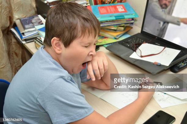 schoolboy studying with video online lesson at home with teache - yawning stock photos et images de collection