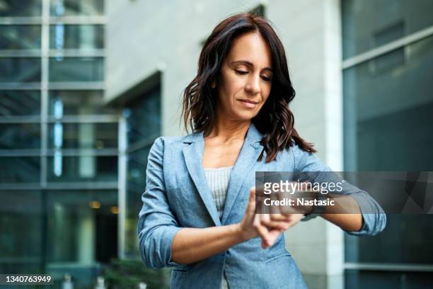 young serious successful business woman looking at her wristwatch outside office building - checking watch stockfoto's en -beelden