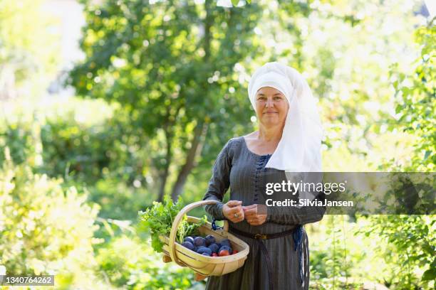 woman wearing medieval dress in garden holding basket with fruit and vegetables - farm worker woman stock pictures, royalty-free photos & images