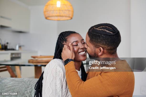 shot of a young man kissing his girlfriend on the cheek while relaxing together at home - black couples kissing stock pictures, royalty-free photos & images