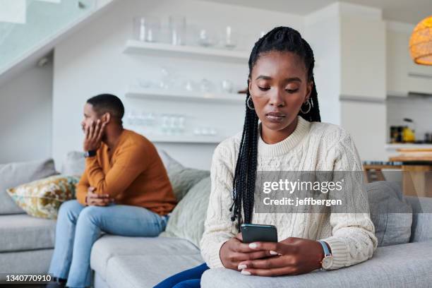 shot of a young woman ignoring her partner while using a cellphone at home - negeren stockfoto's en -beelden