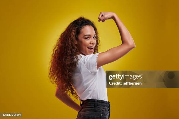 retrato de estudio de una mujer joven flexionando sus bíceps sobre un fondo amarillo - flexionar los músculos fotografías e imágenes de stock