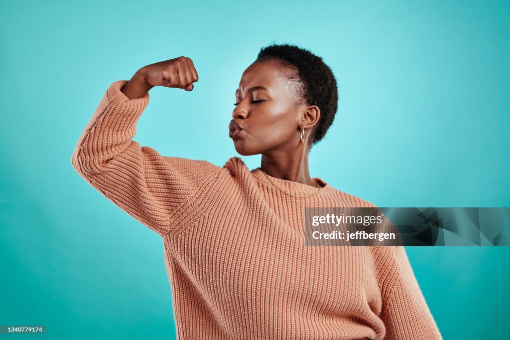 Shot of a beautiful young woman flexing while standing against a turquoise background