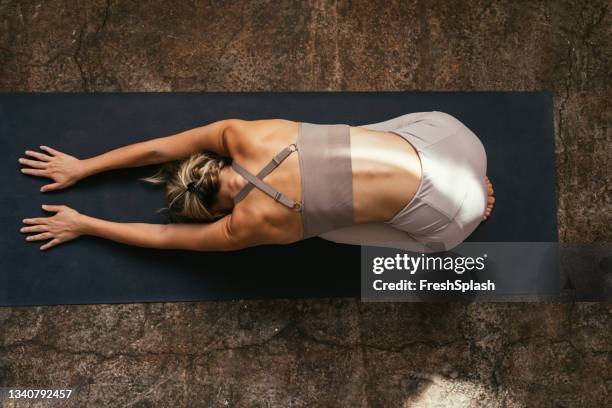 a young caucasian woman stretching on her yoga mat from above - blue leggings stock pictures, royalty-free photos & images