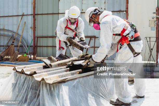 safety is our top priority. workers wearing full body protective clothing while working with the asbestos roof tiles. - asbestos removal photos et images de collection
