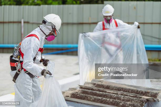 safety is our top priority. workers wearing full body protective clothing while working with the asbestos roof tiles. - asbestos stock pictures, royalty-free photos & images