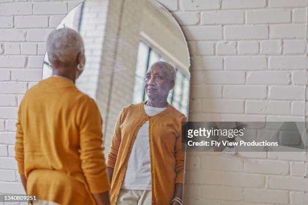 beautiful black senior woman trying on outfit in front of mirror - mirrors stockfoto's en -beelden