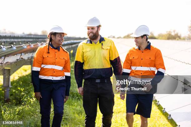 multiracial group of three technicians surrounded by solar panels - multi-cultural minority groups stock pictures, royalty-free photos & images