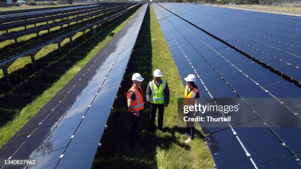 multiracial group of three engineers surrounded by solar panels - solar power station stock pictures, royalty-free photos & images