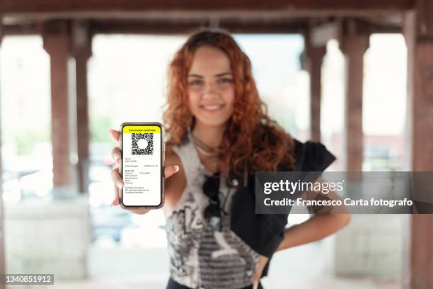 mixed race woman student using digital vaccine passport app in mobile phone - pasar fotografías e imágenes de stock