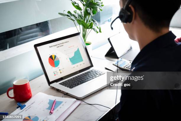 young asian coworker with wireless headphones having business discussion and brainstorming using laptop at his workstation - laptop headset stock pictures, royalty-free photos & images