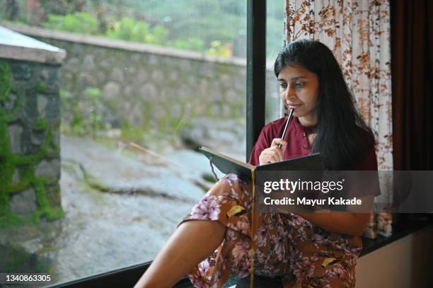 woman writing in a diary sitting at the window - poeta imagens e fotografias de stock