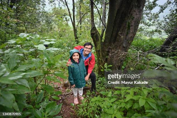 portrait of father and daughter wearing rain jackets in a forest - enjoy monsoon stock-fotos und bilder