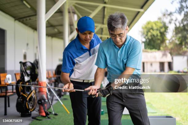 man teaching senior man to play golf - drivingrange stockfoto's en -beelden