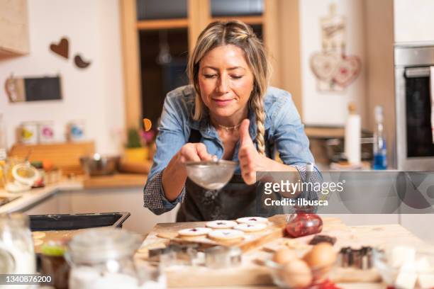 woman baking at home: adding icing sugar on cookies - baking cookies stock pictures, royalty-free photos & images