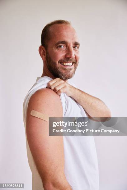 smiling man with a bandage on his arm after a covid-19 vaccination - man studio shot stock pictures, royalty-free photos & images