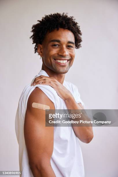 lächelnder afroamerikaner mit verband am arm nach einer covid-19-impfung - studio shot stock-fotos und bilder