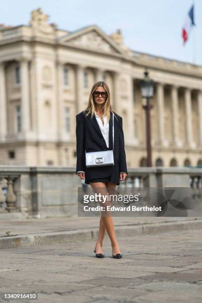 Actress Sveva Alviti wears a black oversized blazer jacket, a white shirt, a black mini skirt, a silver shiny rectangular leather bag " Viv' Choc "...