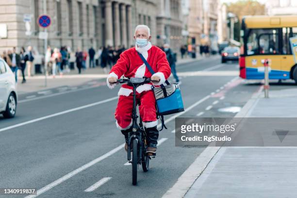 santa delivery man with a face mask delivering orders on a bike - santa riding stock pictures, royalty-free photos & images