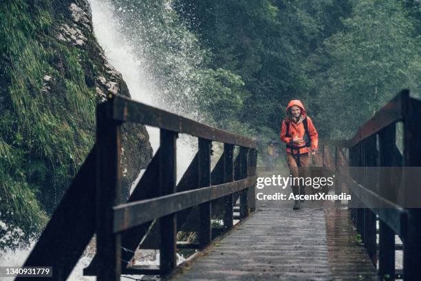 young man hikes across bridge near flowing waterfall - pantalon stockfoto's en -beelden