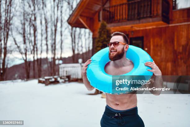 smiling bearded male putting inflatable beach donut over head while standing in snow - weird hobbies stock pictures, royalty-free photos & images