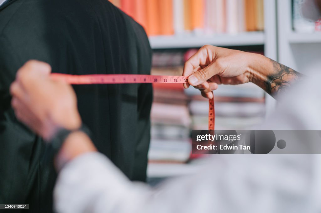 Close up asian chinese senior man tailor measuring his client's body size for new blazer making at studio