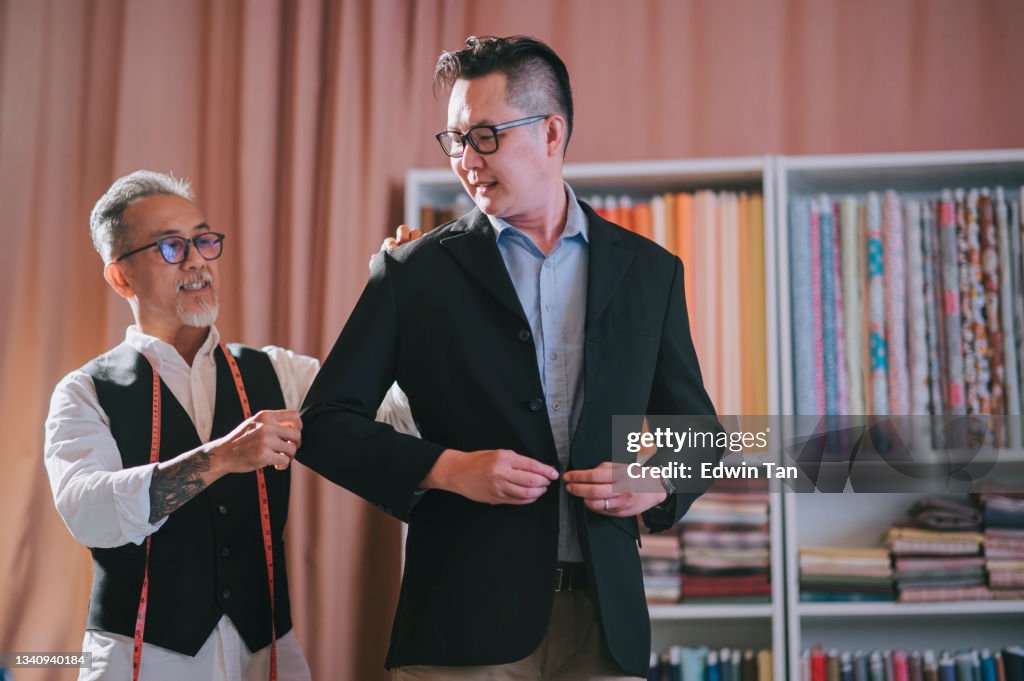 Asian chinese senior man tailor helping his client trying on new tailored blazer suit at his studio