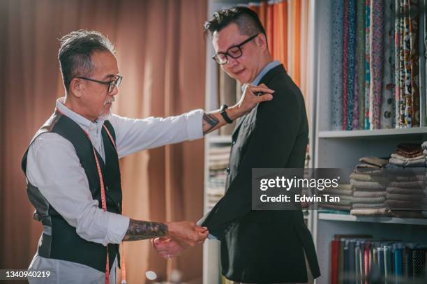 asian chinese senior man tailor helping his client trying on new tailored blazer suit at his studio - custom tailored suit stock pictures, royalty-free photos & images