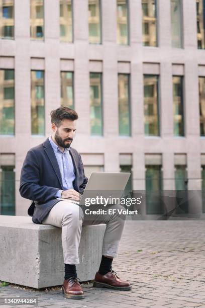 trendy businessman in elegant suit working on laptop outdoors in business center - cool modern mann büro business stock-fotos und bilder
