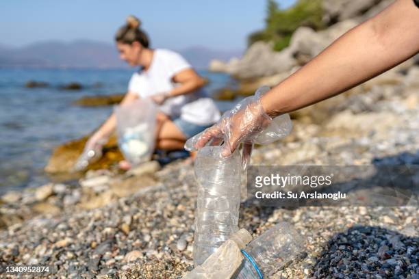 deux femmes bénévoles ramassent les déchets plastiques jetés au bord de la mer - volunteer beach photos et images de collection