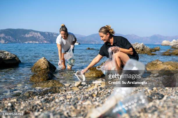 two volunteer women collect discarded plastic waste by the sea - lifting stockfoto's en -beelden