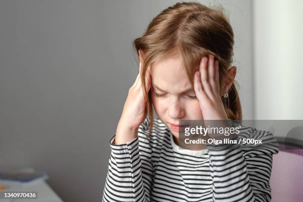 young girl with headache sitting at table at home - headache child fotografías e imágenes de stock