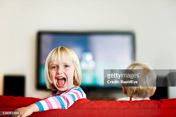 little girl turns back from television and shouts excitedly - family watching tv from behind stockfoto's en -beelden