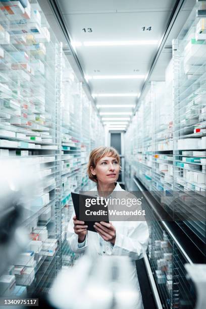 female pharmacist holding digital tablet while searching medicine at medical store - pharmaceutical industry stock pictures, royalty-free photos & images