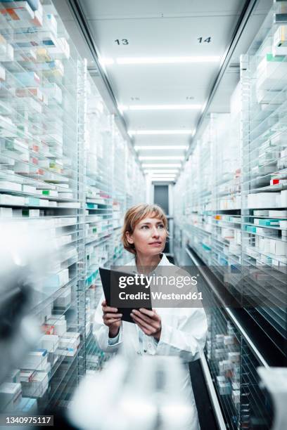 female pharmacist holding digital tablet while searching medicine at medical store - female pharmacist with a digital tablet imagens e fotografias de stock