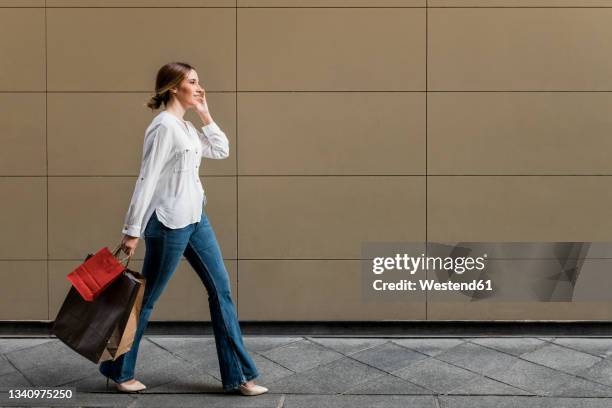 woman looking away while walking with shopping bags on footpath - side view carrying stock pictures, royalty-free photos & images