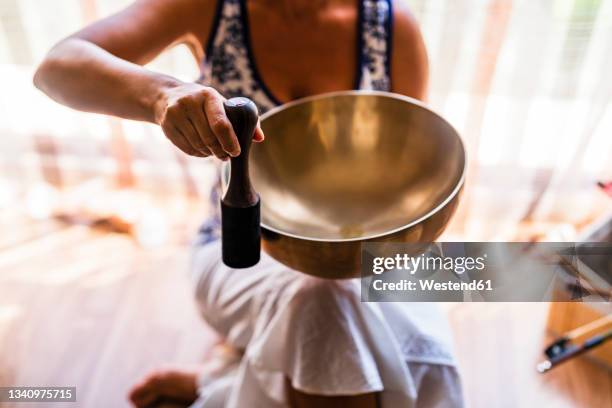 female sound therapist playing brass bowl with mallet in studio - percussion mallet stock-fotos und bilder