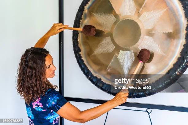 female sound therapist playing gong with mallets in studio - music therapy stock pictures, royalty-free photos & images